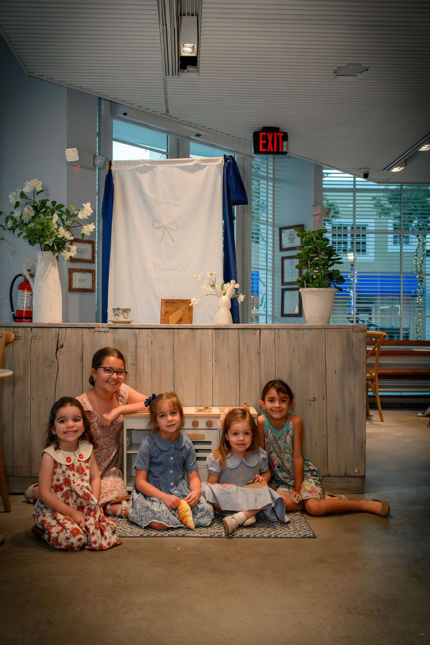 Group of young girls posing together at a bridal shower event in front of a decorated backdrop.