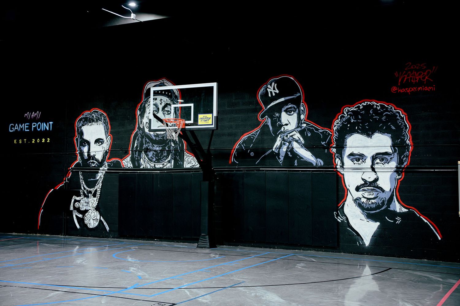 Indoor basketball court mural featuring black and white portraits of four figures with red accents and Game Point text on dark walls.