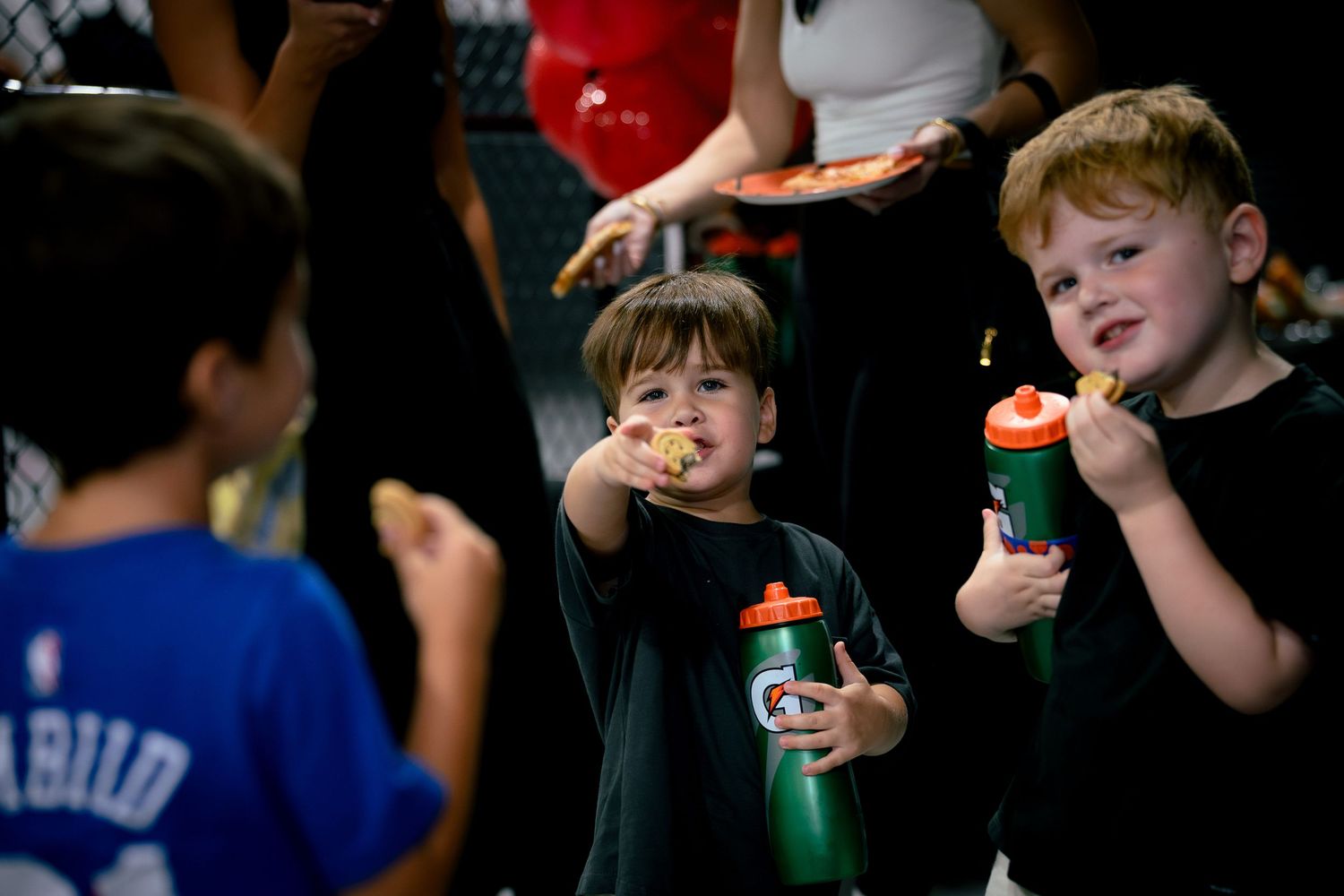 Children eating pizza and holding Gatorade bottles at a youth sports event, smiling and enjoying snacks.