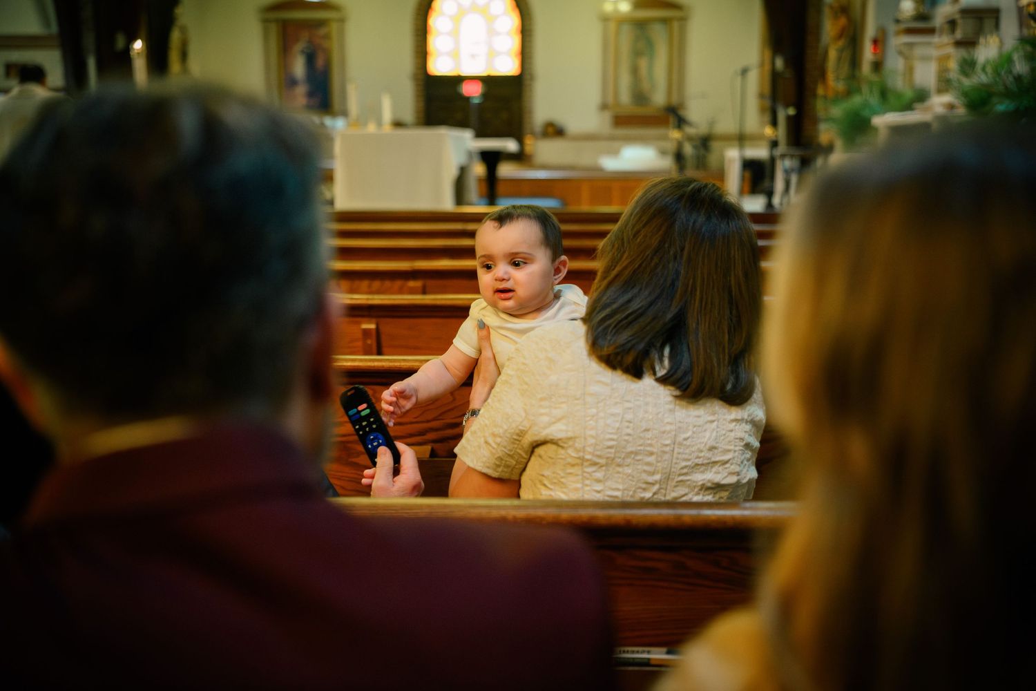 A person in profile sits in a church pew during a religious service with soft lighting and wooden details.