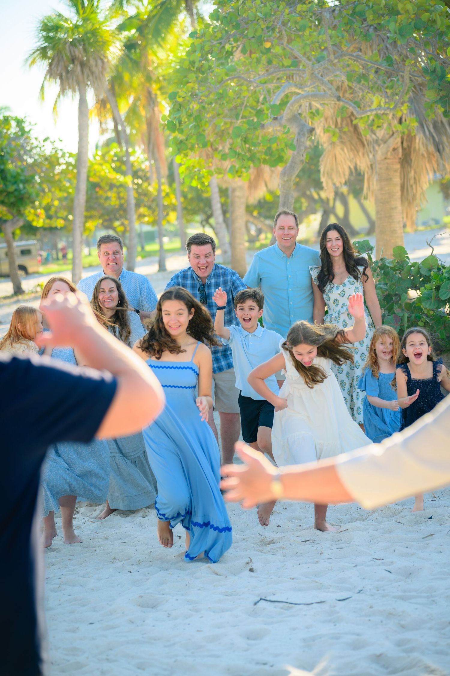 Group in coordinated blue outfits enjoying a candid beach photo session at sunset with palm trees in background.