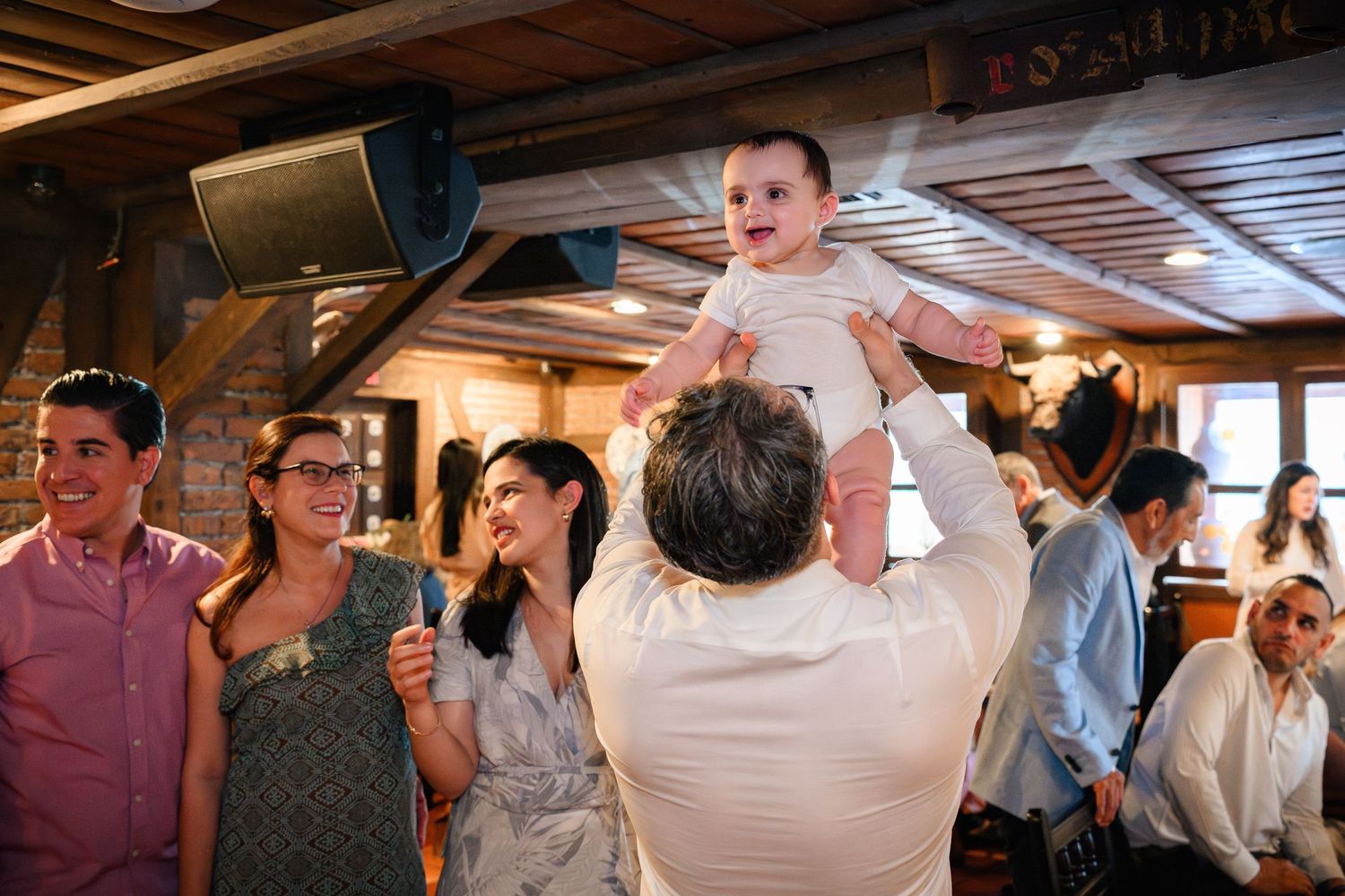 A baby being lifted into the air during a Baptism lunch hosted at Casa Juancho in Pequeña Habana, Miami, FL.