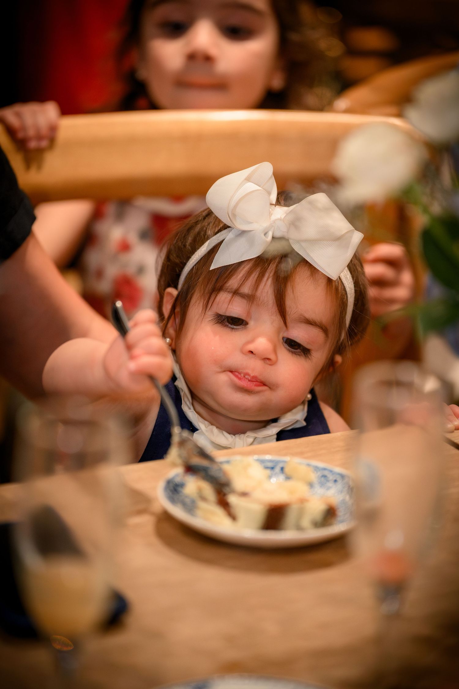 A sequence of images showing a small child in a white bow leaning over a plate of food at a dining table.