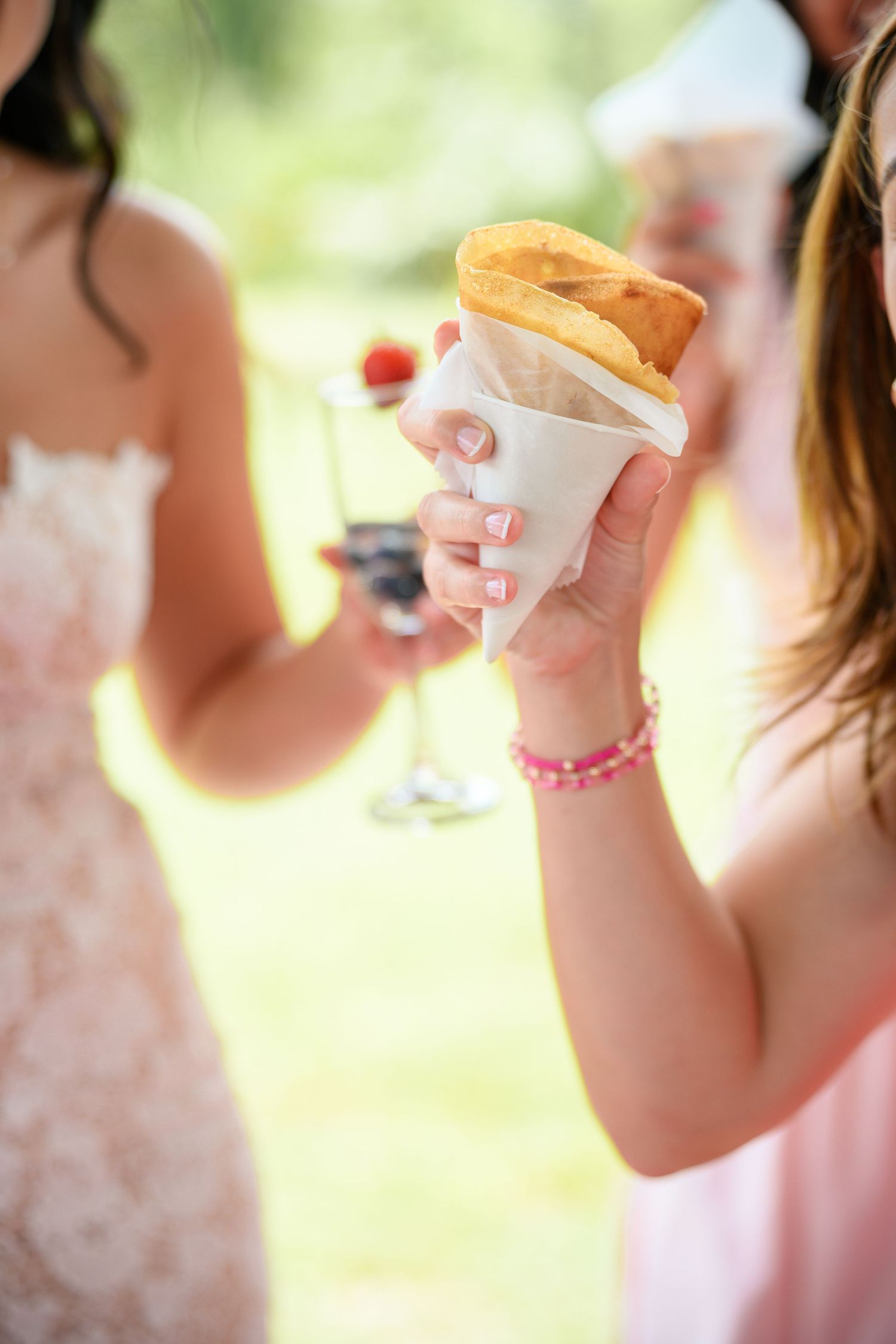 Bridesmaids in pink dresses hold ice cream cones during a wedding celebration outdoors.