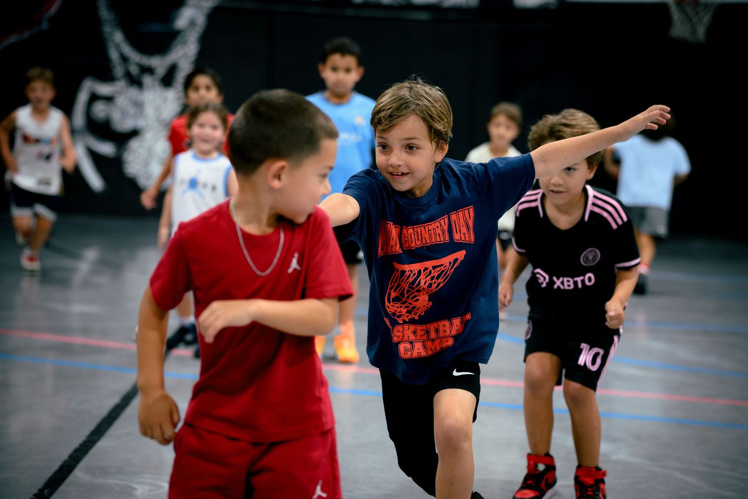 Young children playing basketball in a gym during a youth basketball camp game.