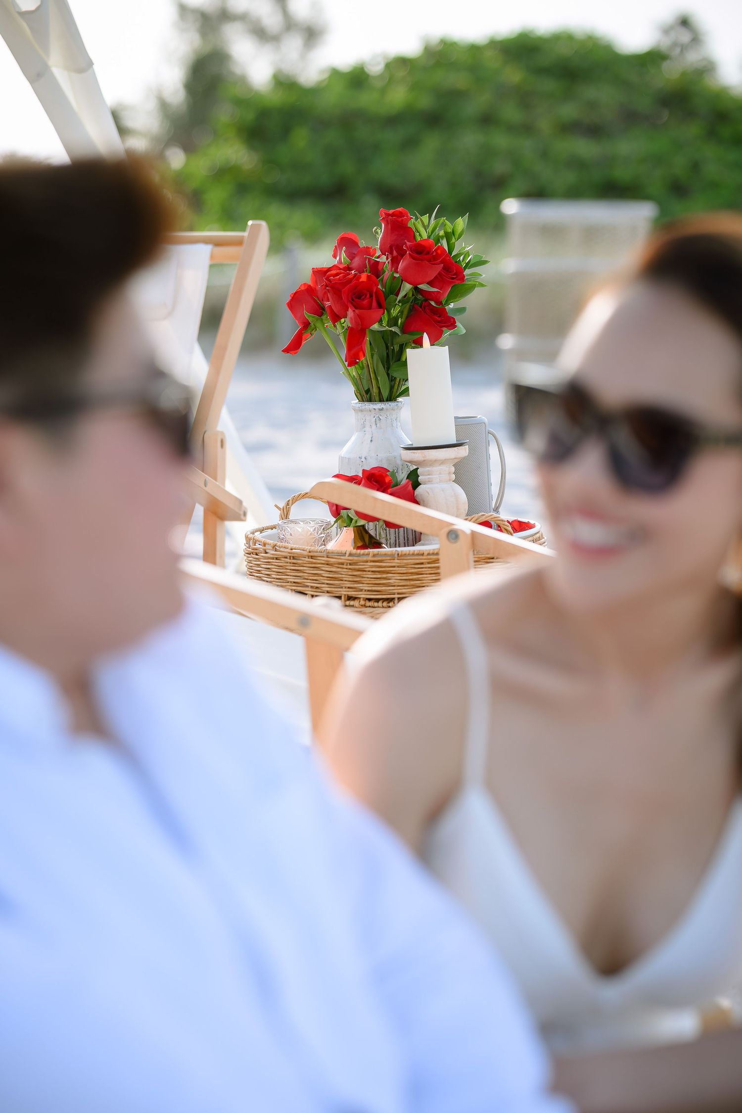 Couple relaxing outdoors with red flowers and picnic basket on a sunny day near the beach.