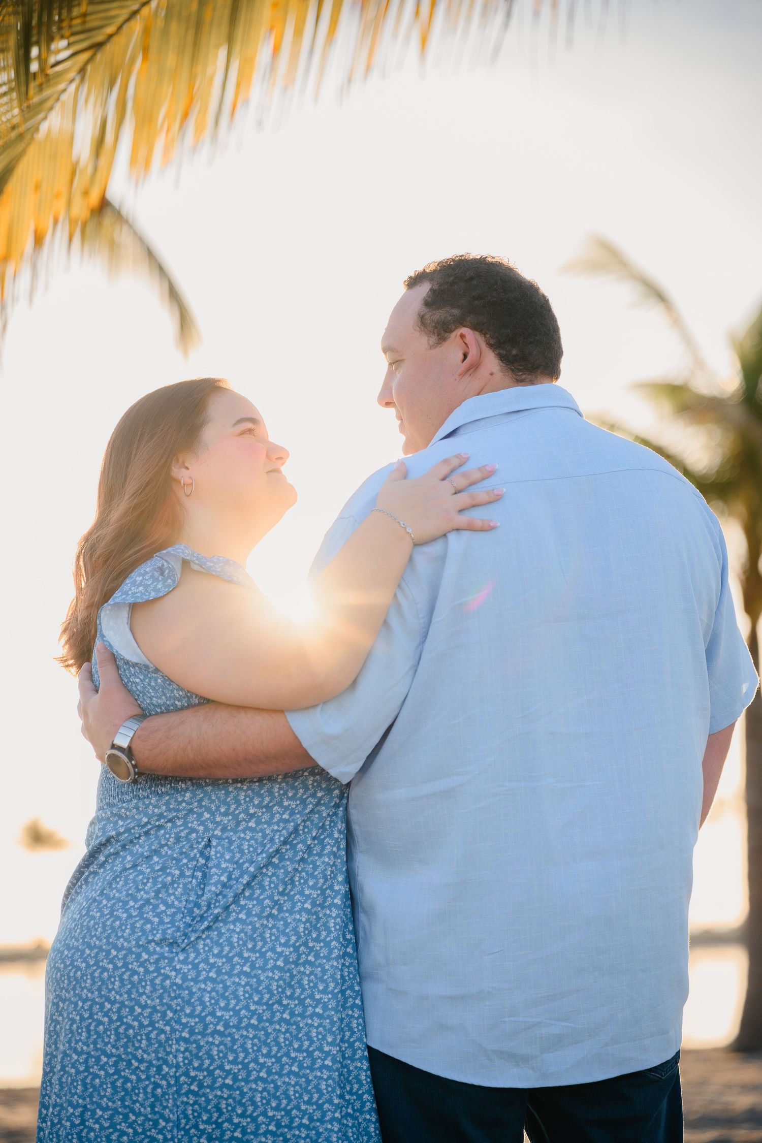 A couple embraces on a tropical beach at golden sunset under swaying palm trees.