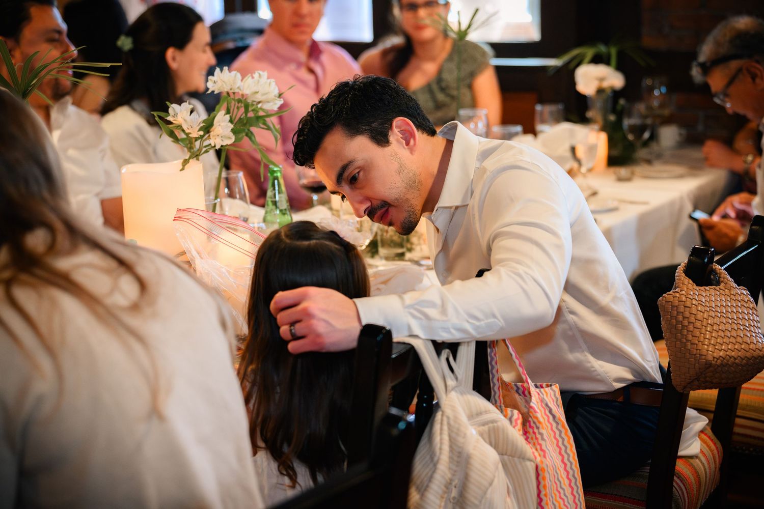 A guest in a white shirt rests their head on a table during an elegant candlelit dinner event.