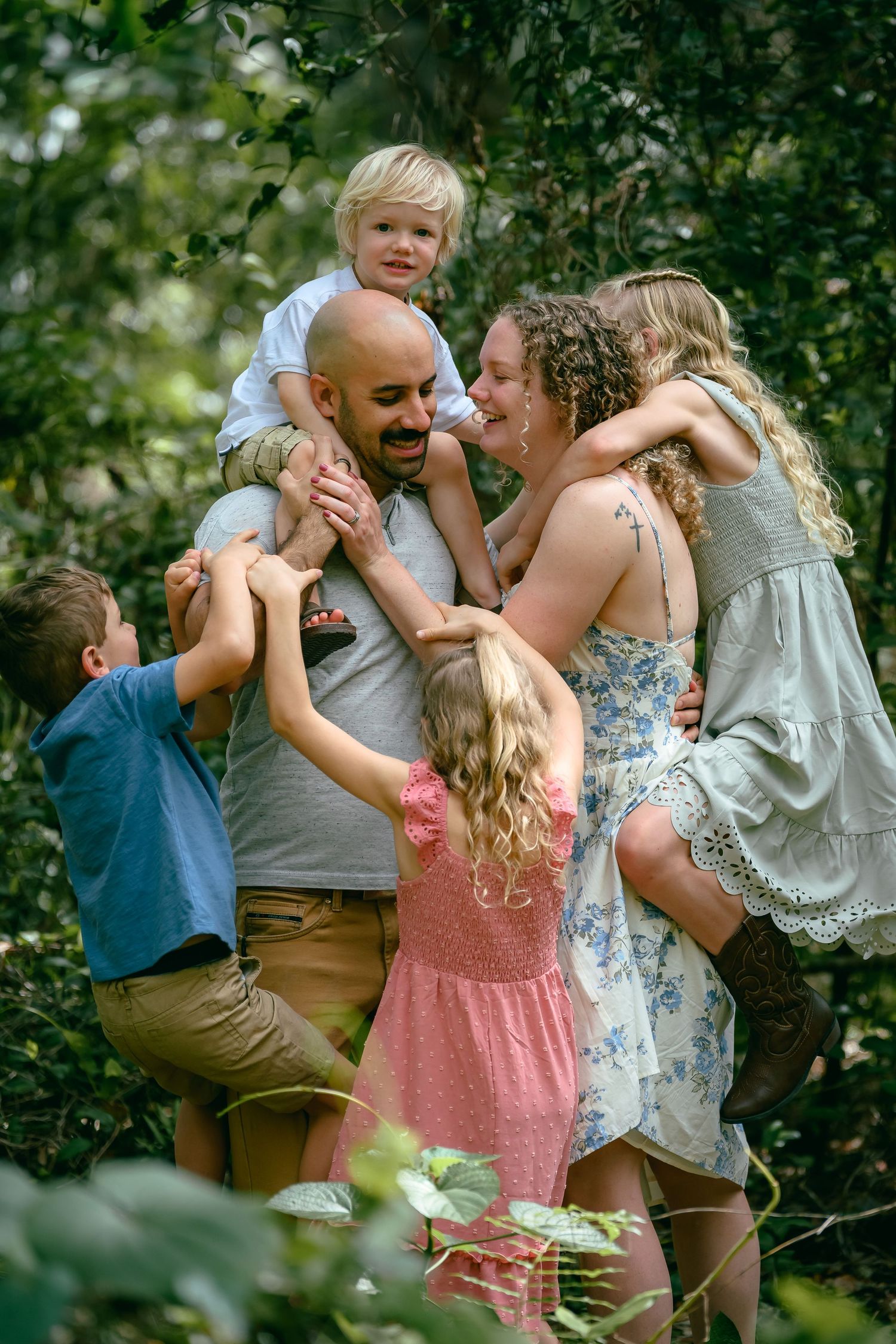 A joyful family with four children hugging their parents outdoors in a lush green garden setting.