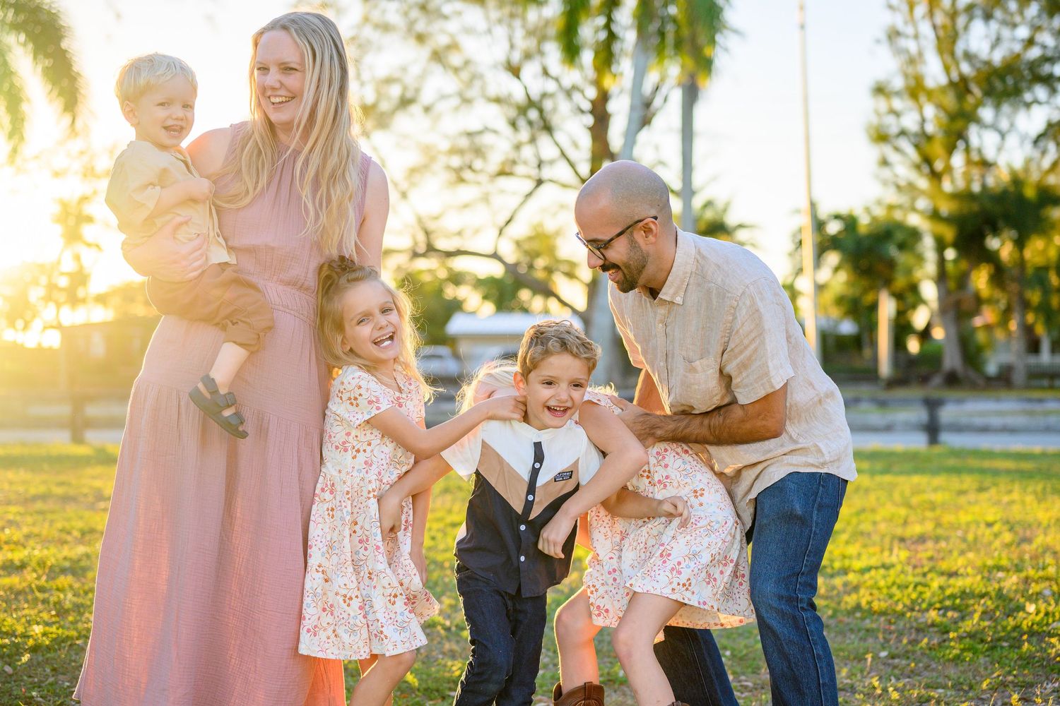 A family shares tender moments together in a sunlit park during golden hour.