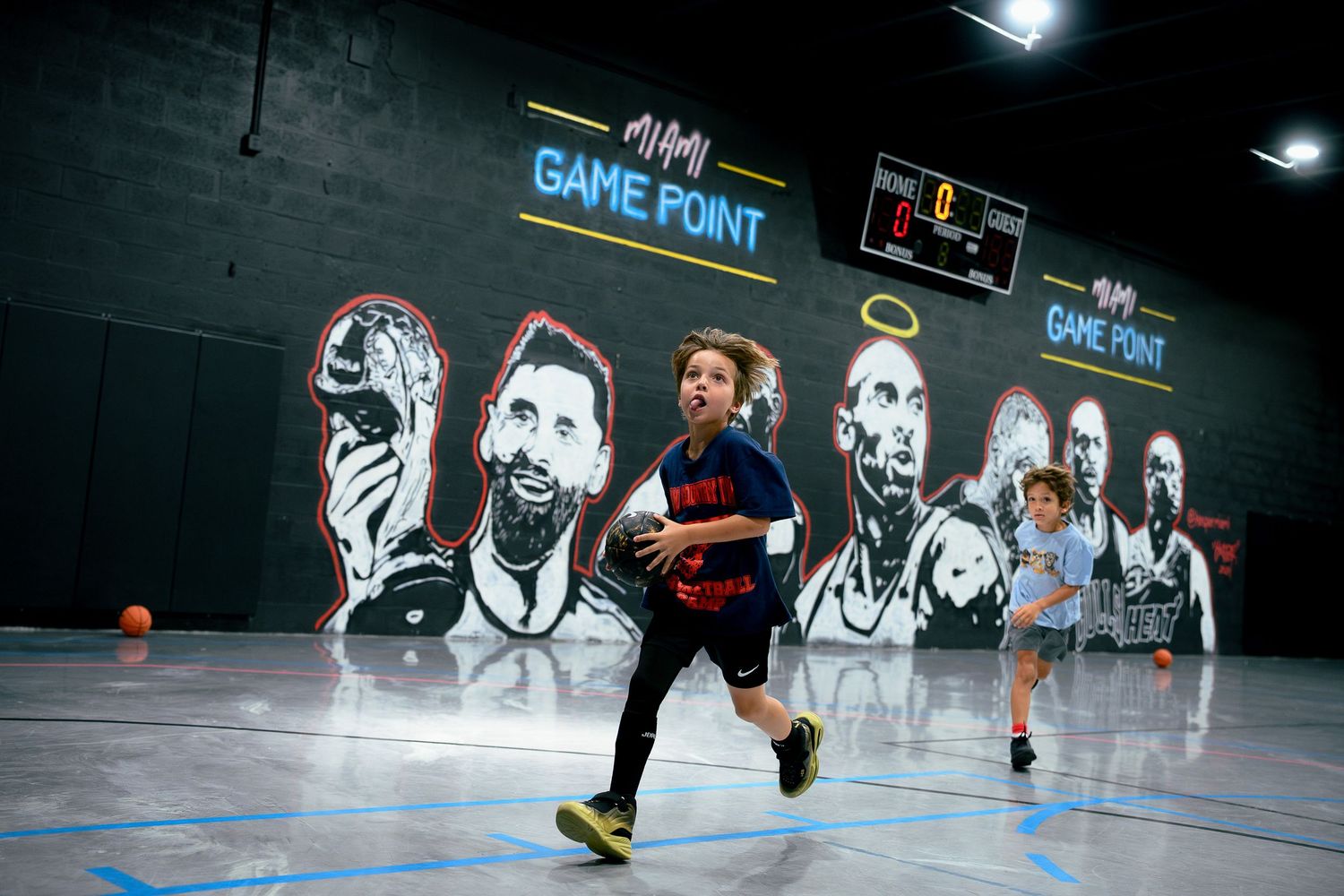 Children playing basketball indoors at Game Point facility featuring large sports murals on dark walls.