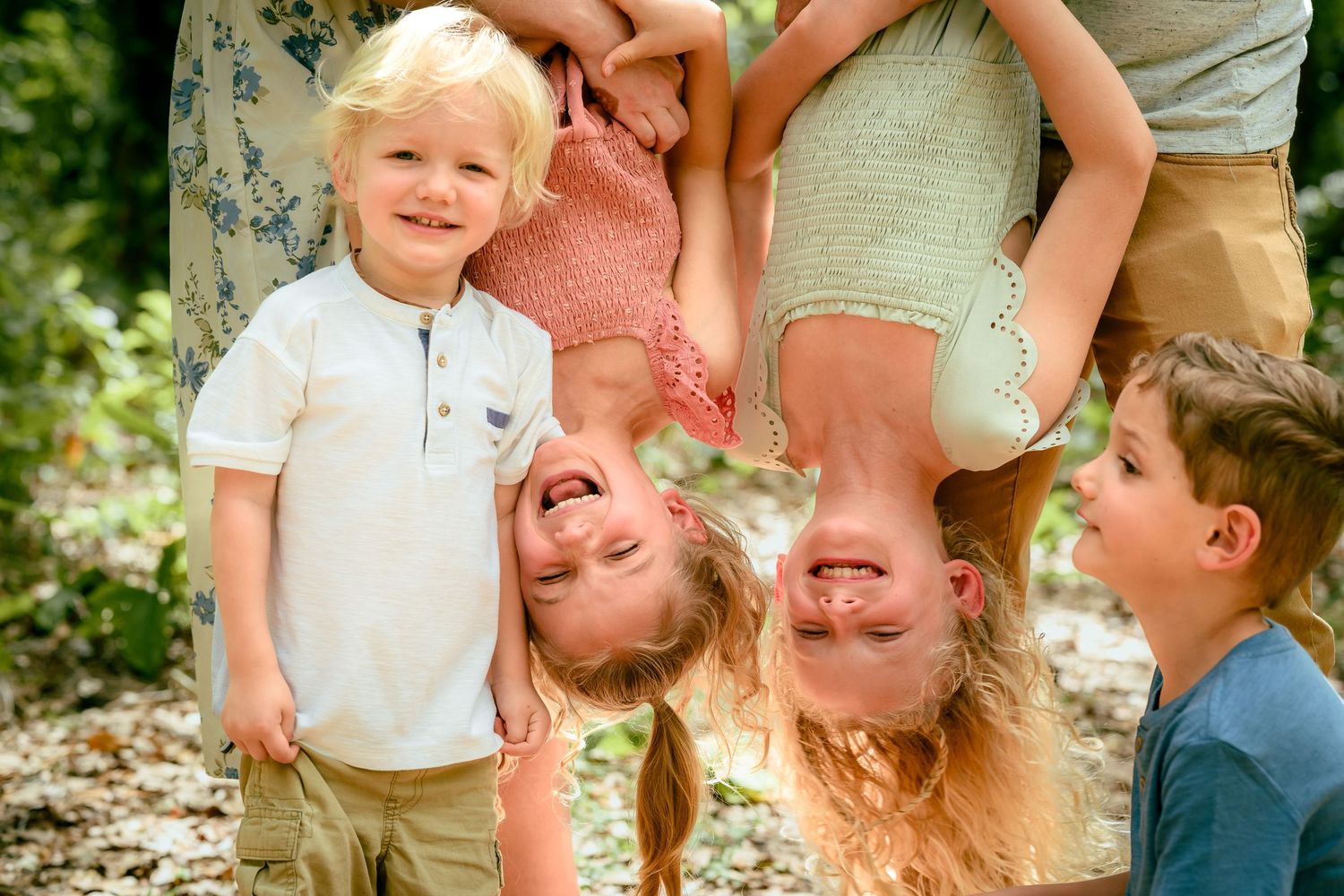 Four happy children playing outdoors, two upside down, smiling in a sunny garden setting.