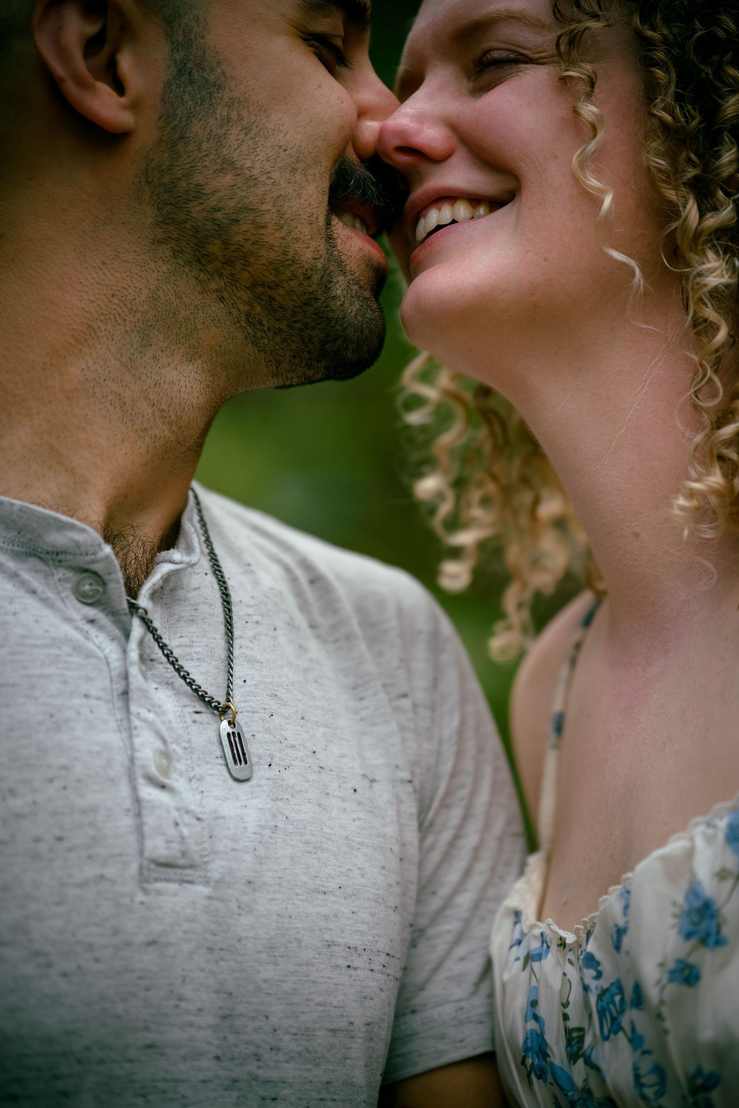 A couple shares a romantic moment, nearly kissing, as the curly-haired woman smiles joyfully outdoors.