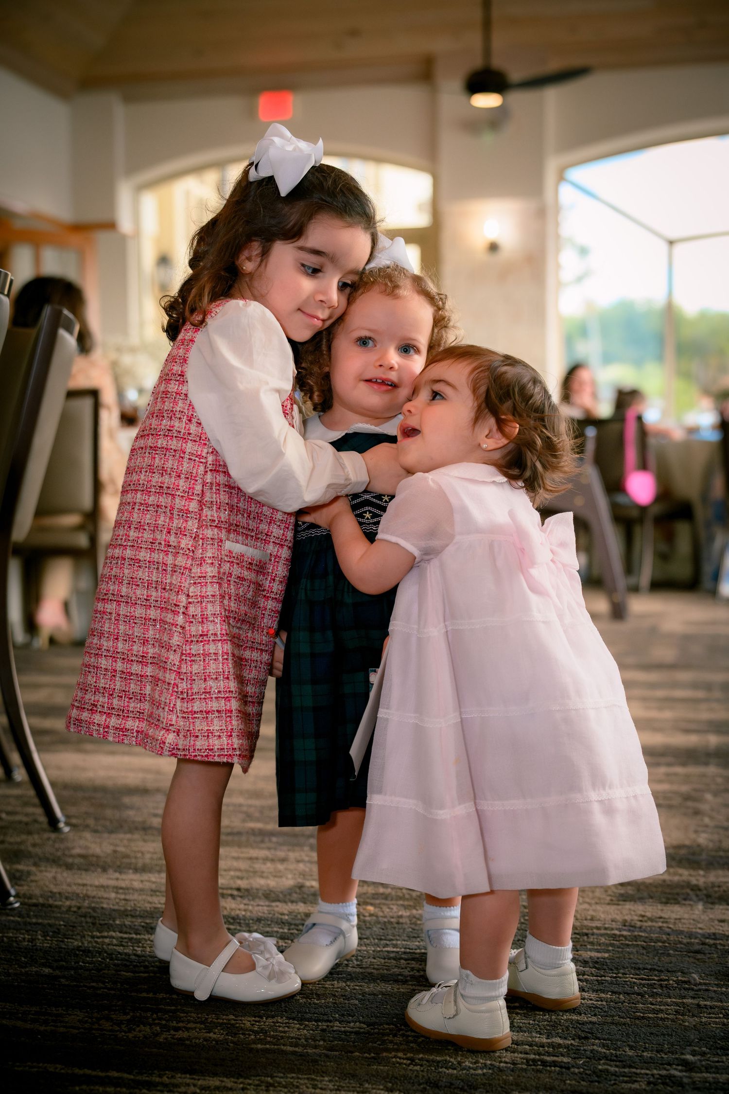 Three adorable little girls in formal dresses posing together at a baby shower celebration.