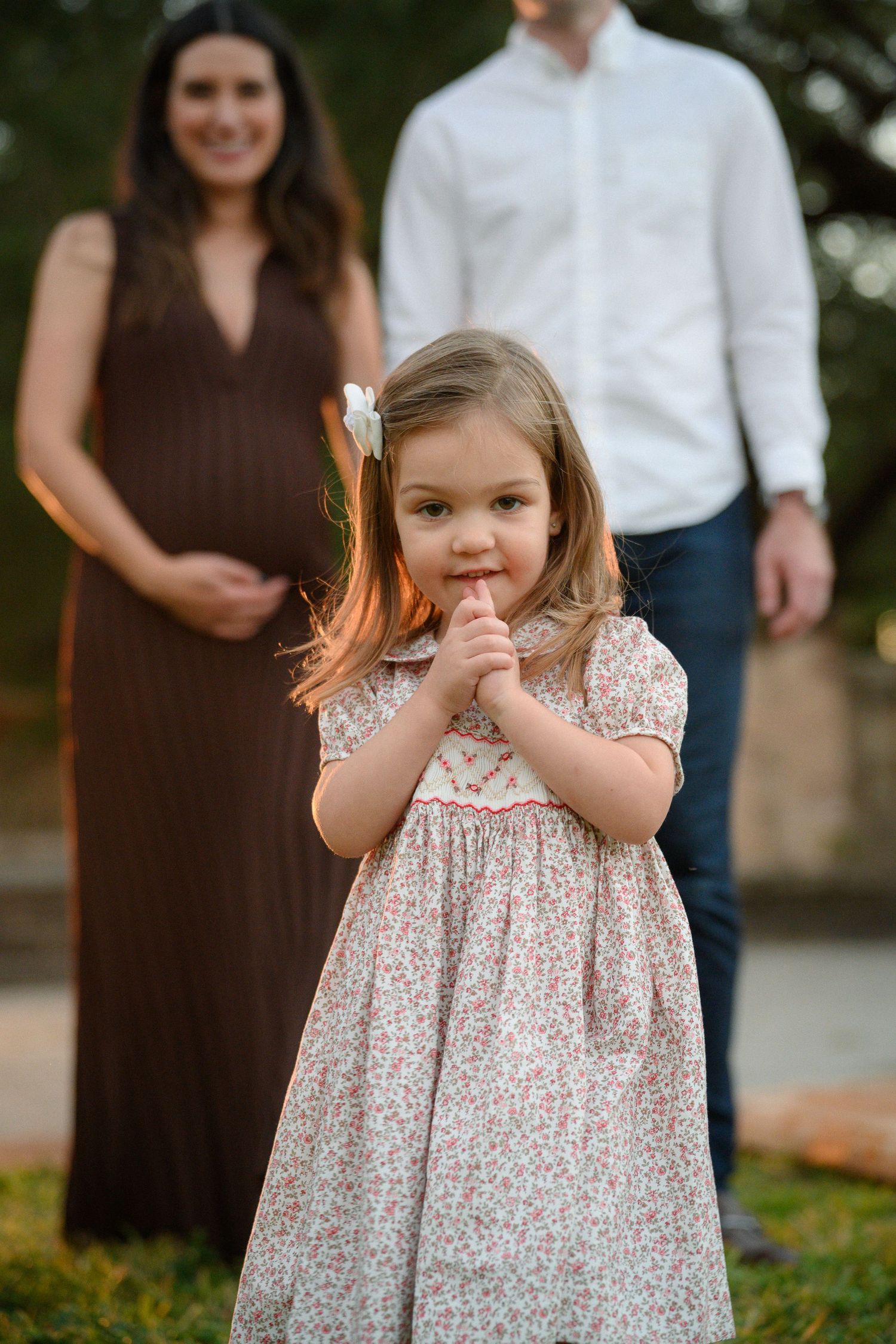 A series of photos showing a young child in a floral dress posing playfully outdoors with family members in brown and white.