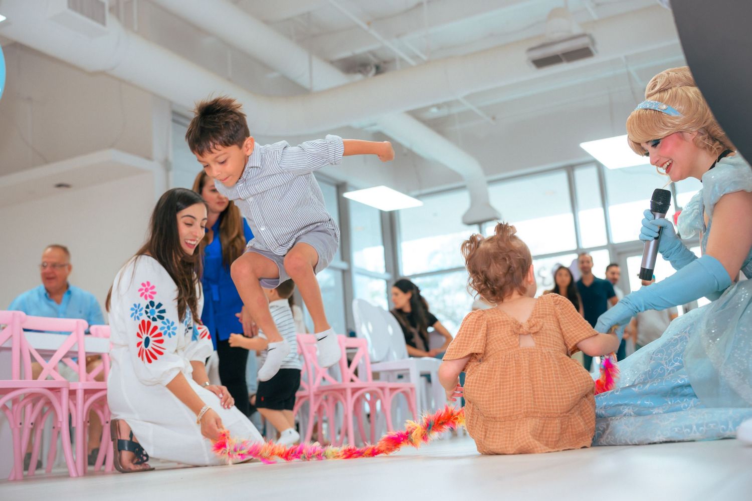 Children playing at a colorful indoor party with a Cinderella character and decorated pink chairs.