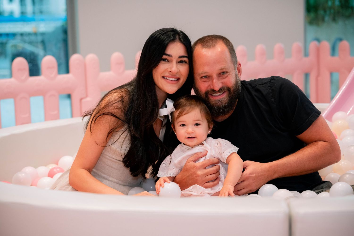 A series of family photos showing tender moments between parents and their newborn baby in soft pink lighting.