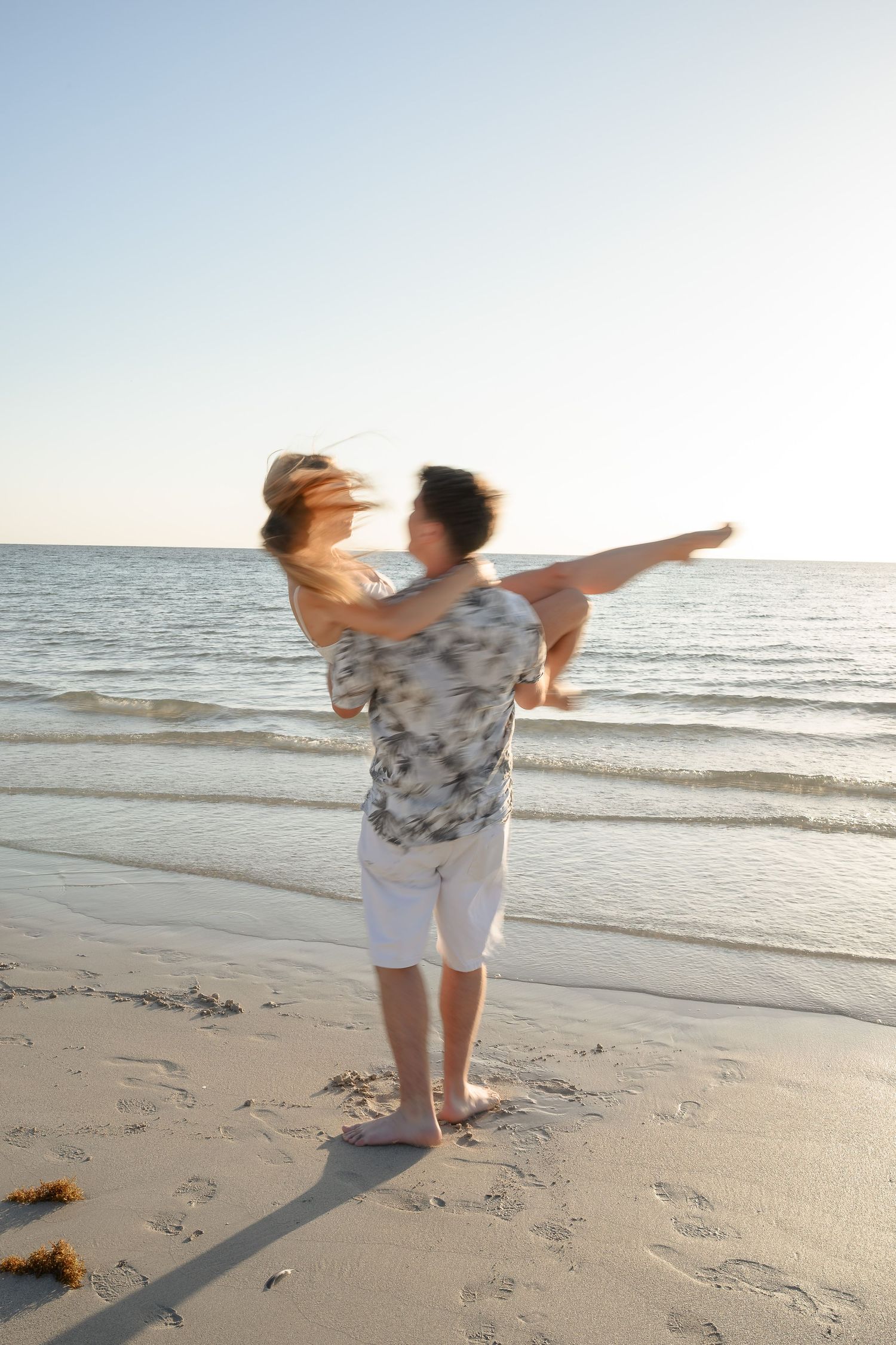 Couple joyfully spinning on a sandy beach at sunset, with ocean waves in the background.