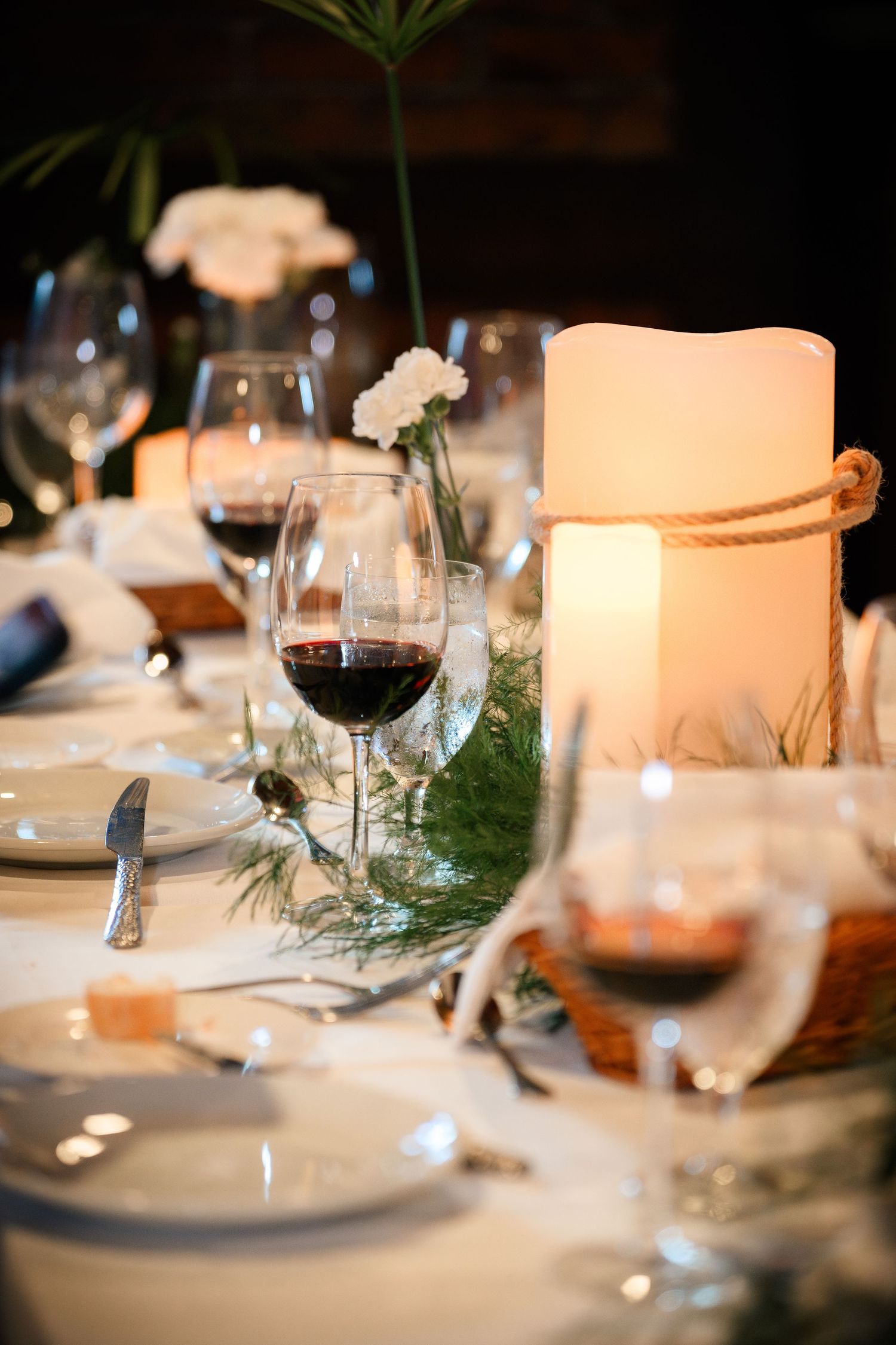 Elegant table settings at a wedding reception with glowing candles, wine glasses, and evergreen sprigs as decor.