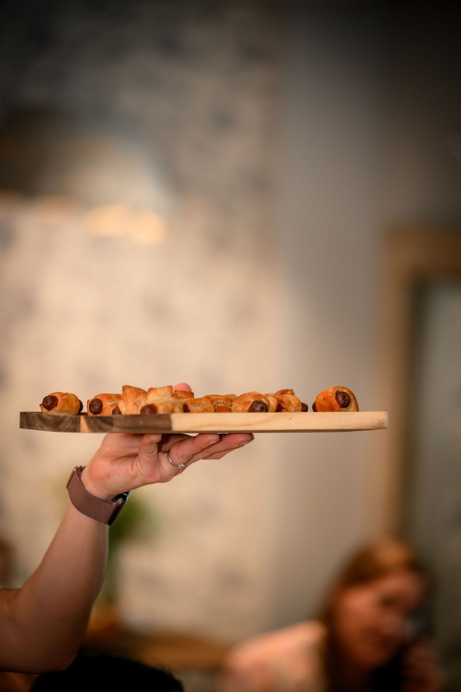 A hand holds up a wooden board displaying freshly rolled cinnamon rolls in a line against a blurred background.
