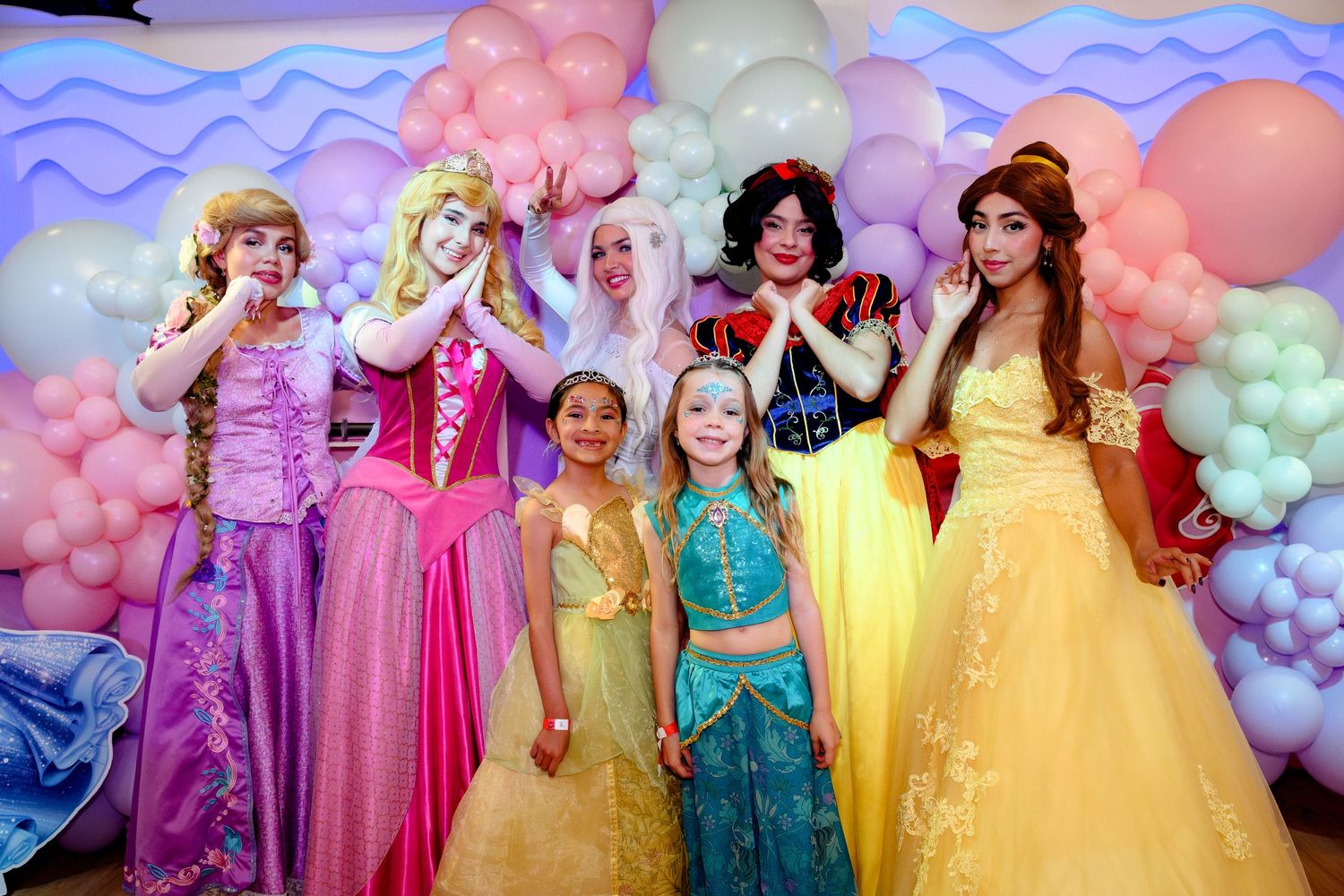 Two birthday girls in princess costumes posing with five Disney princess character performers.