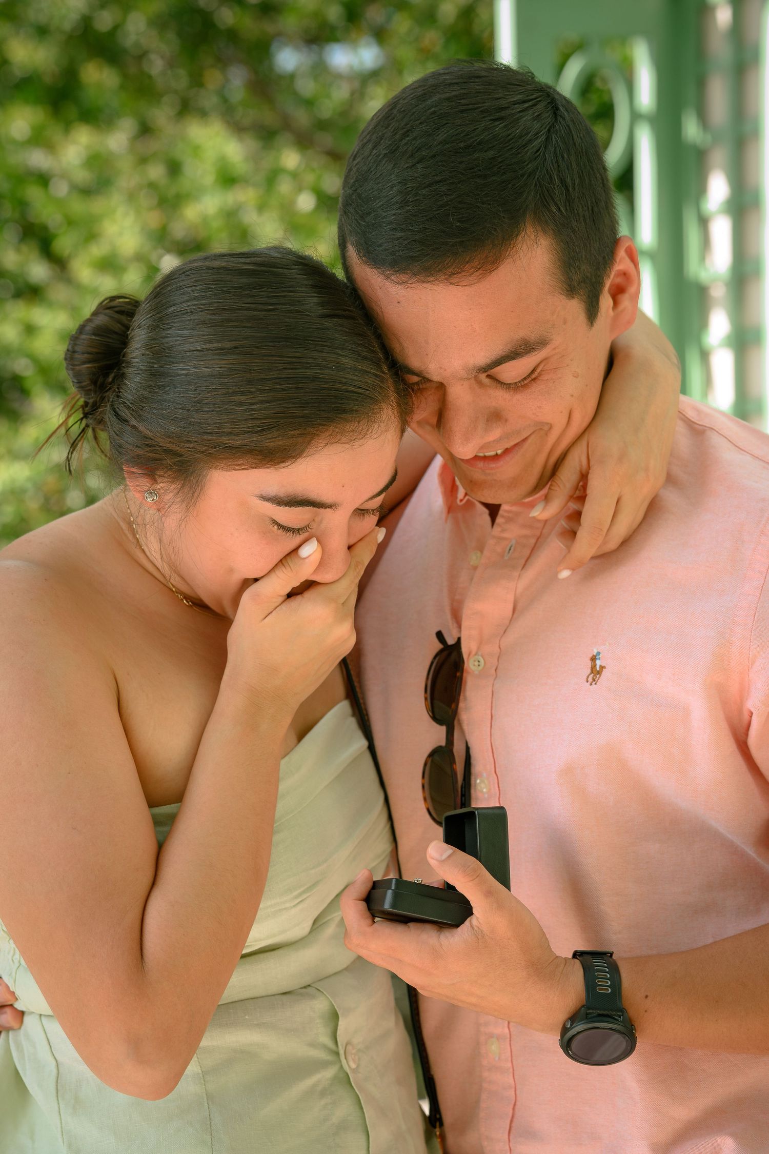 Emotional couple sharing a marriage proposal moment, man holding open ring box while woman covers her mouth in tears.
