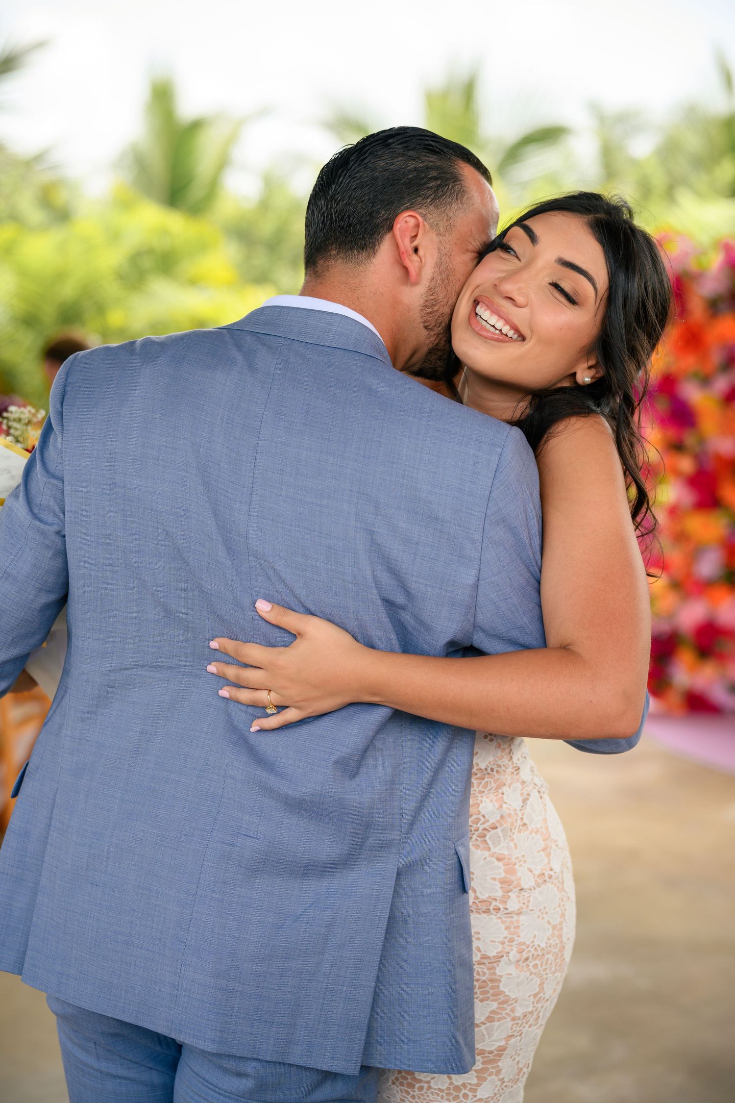 A couple shares an intimate embrace during their outdoor wedding ceremony with vibrant tropical flowers in the background.
