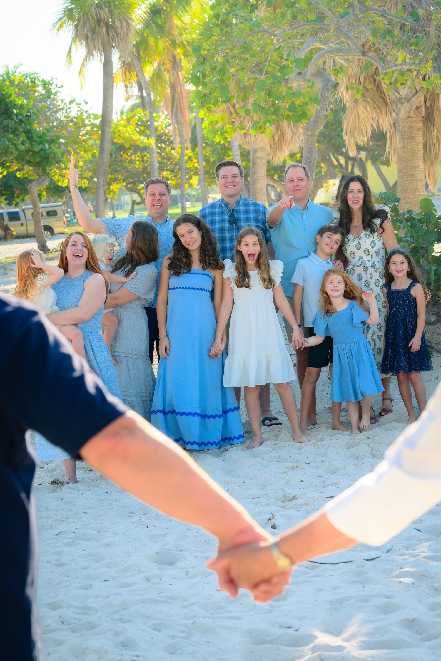 A group photo session on a sandy beach with people wearing coordinated blue and white outfits in natural sunlight.