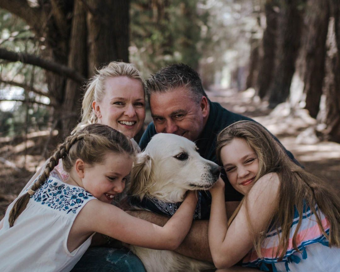 Family cuddling their dog in a forest setting, warm and relaxed family photography session