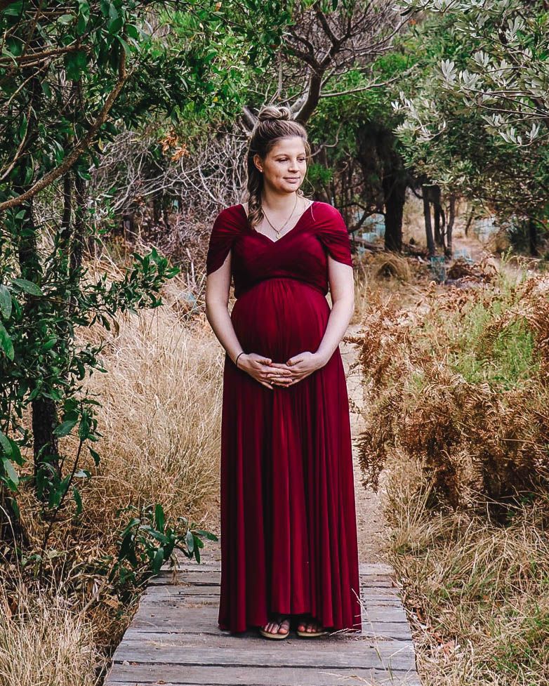 Maternity photography session outdoors, pregnant woman in red dress surrounded by nature