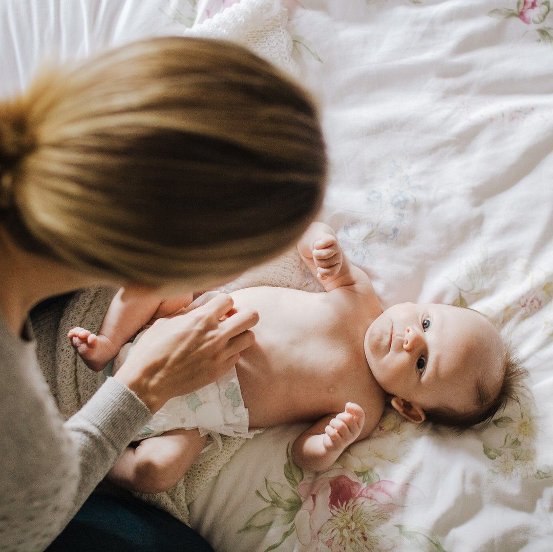 Mother gently holding baby on bed, soft natural light newborn photography