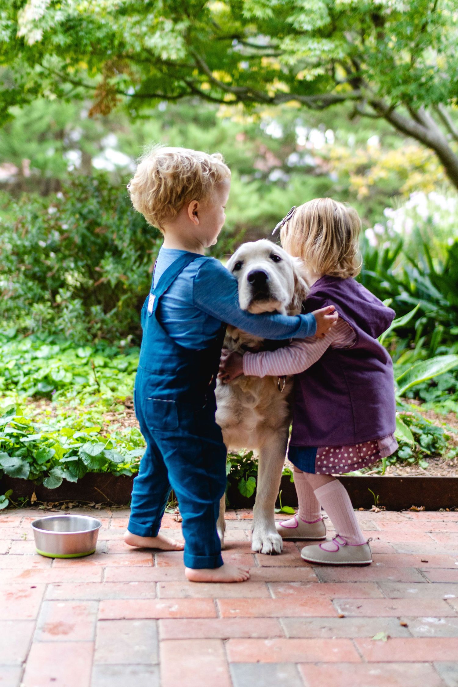 Two young children hugging in a garden setting, candid family photography capturing connection and emotion