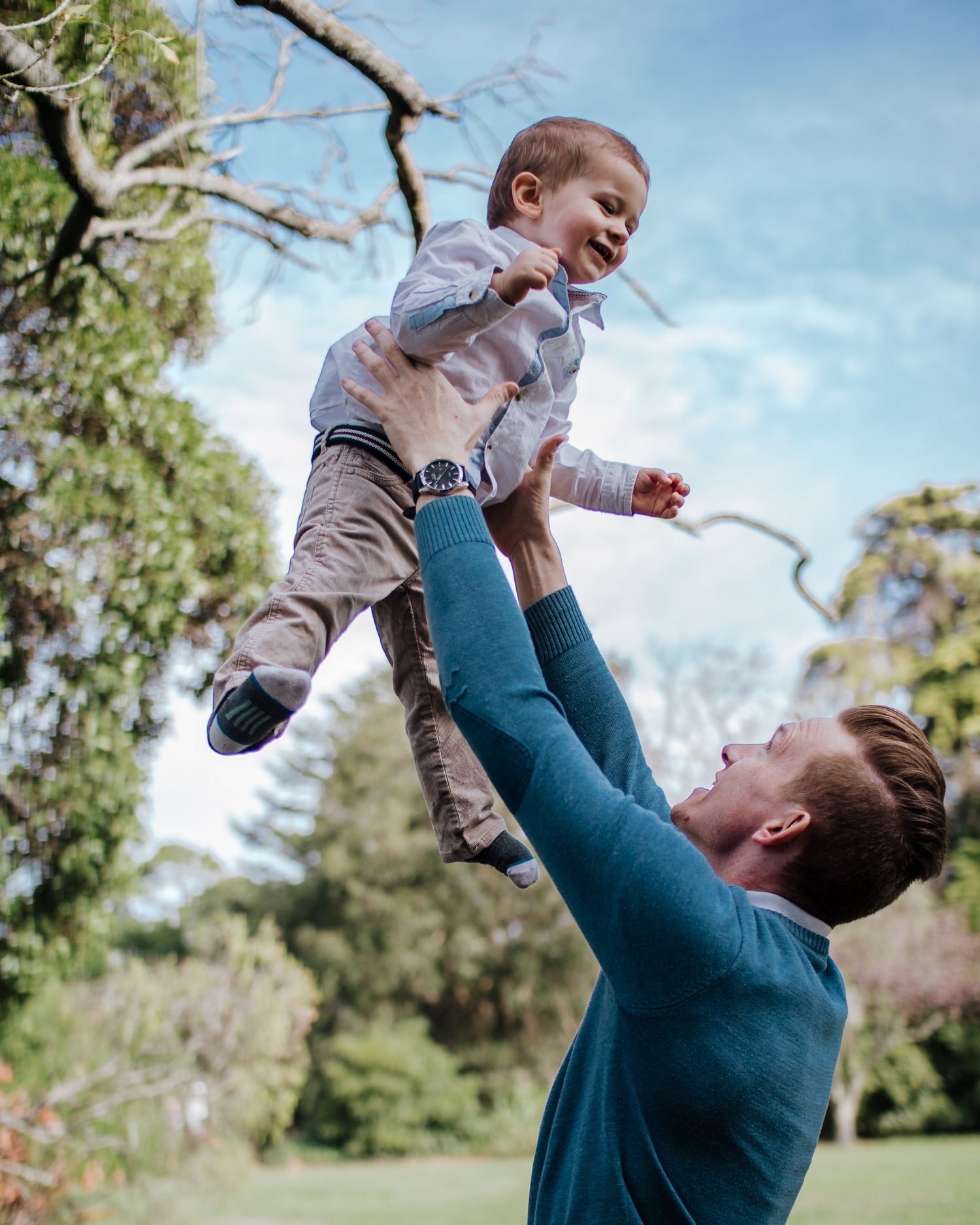 Father lifting child into the air outdoors, playful candid family photography moment
