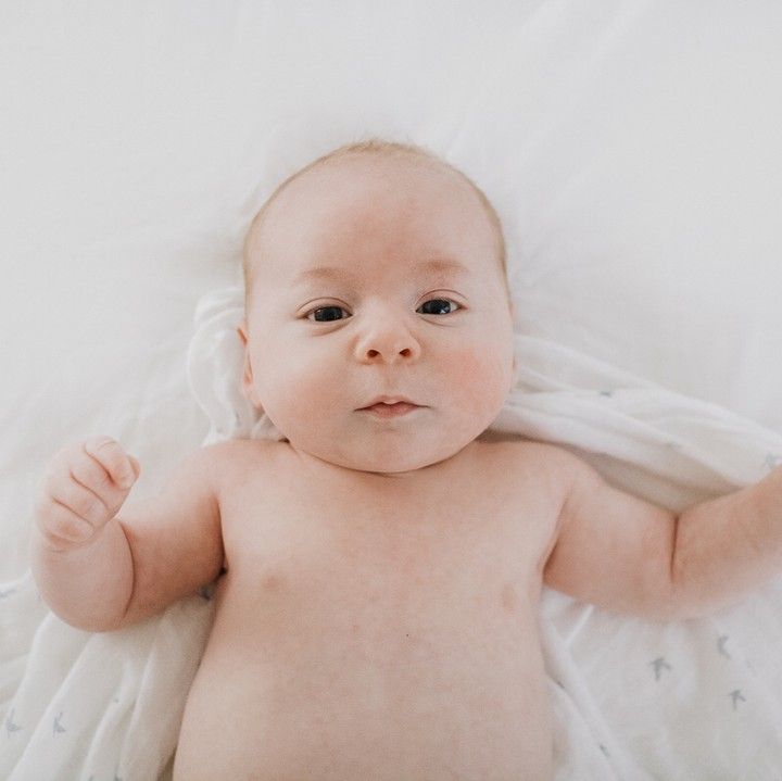 Newborn baby lying on soft white bedding, simple and natural newborn photography