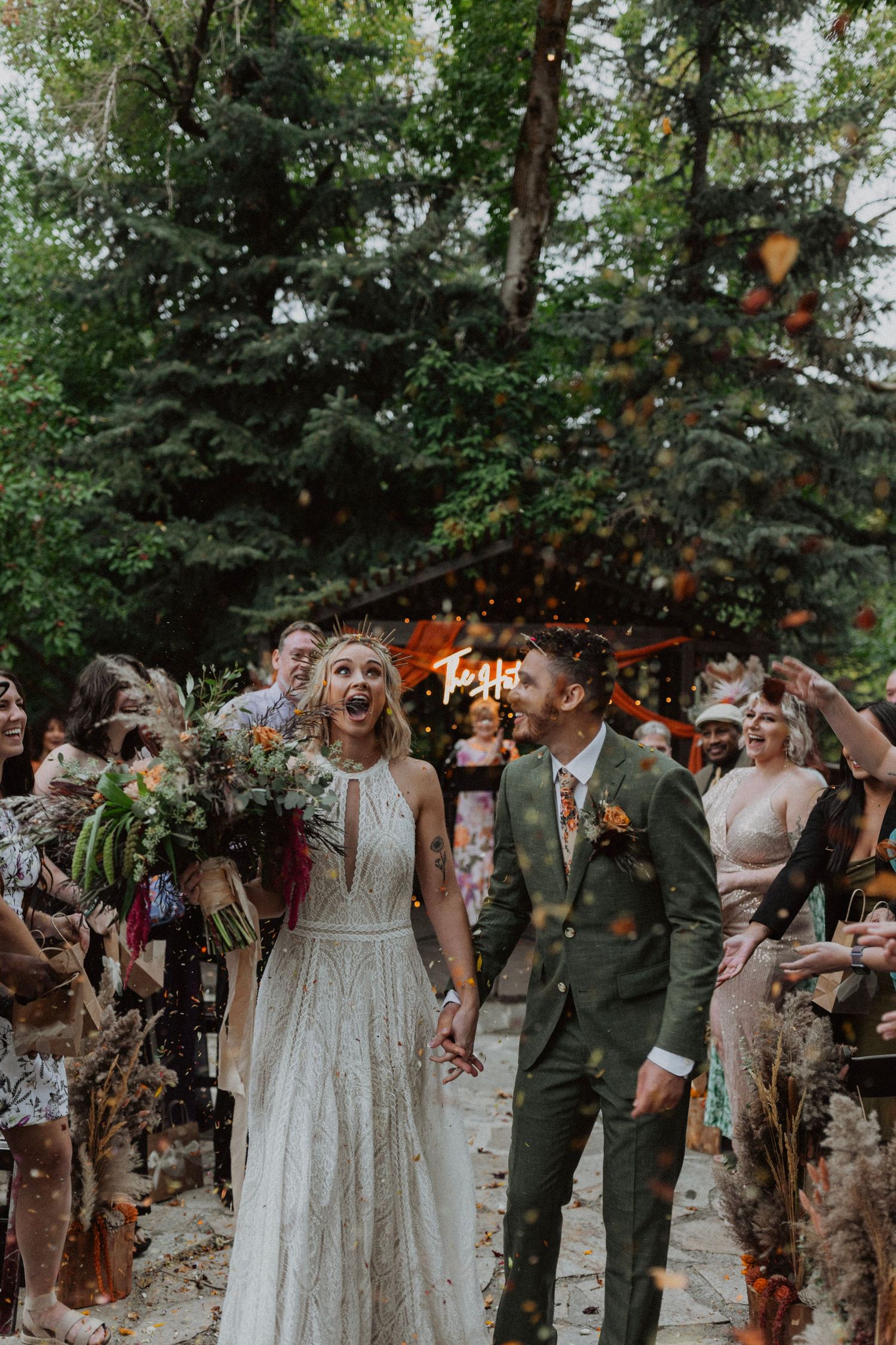 Joyful bride and groom walk down the aisle as guests toss orange confetti at an outdoor forest wedding in Montana Glacier National Park.