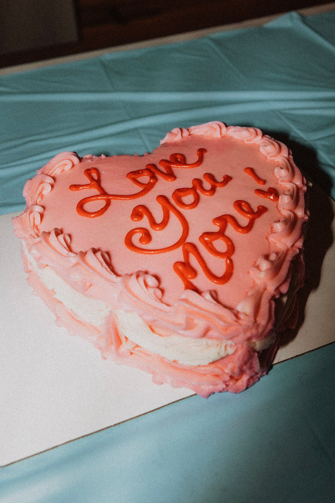 Heart-shaped pink wedding cake decorated with red frosting script reading Love You More in Montana Glacier National Park.