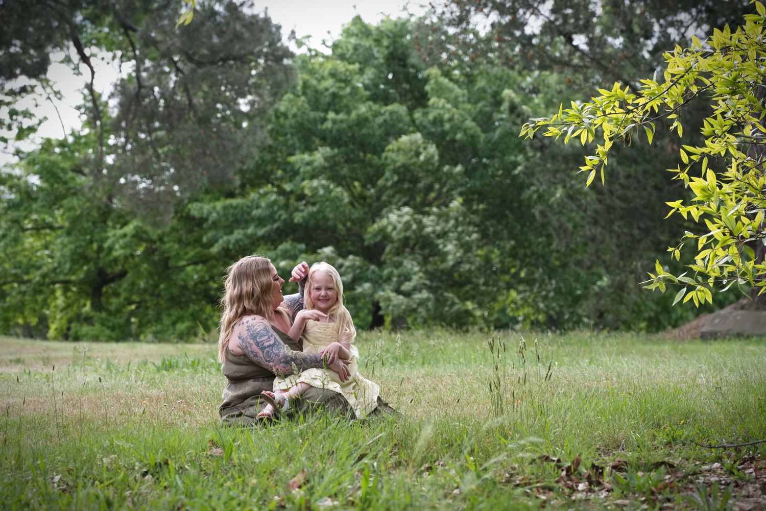 Mother and daughter sitting together in a grassy park, photographed by Wren & I Photography.