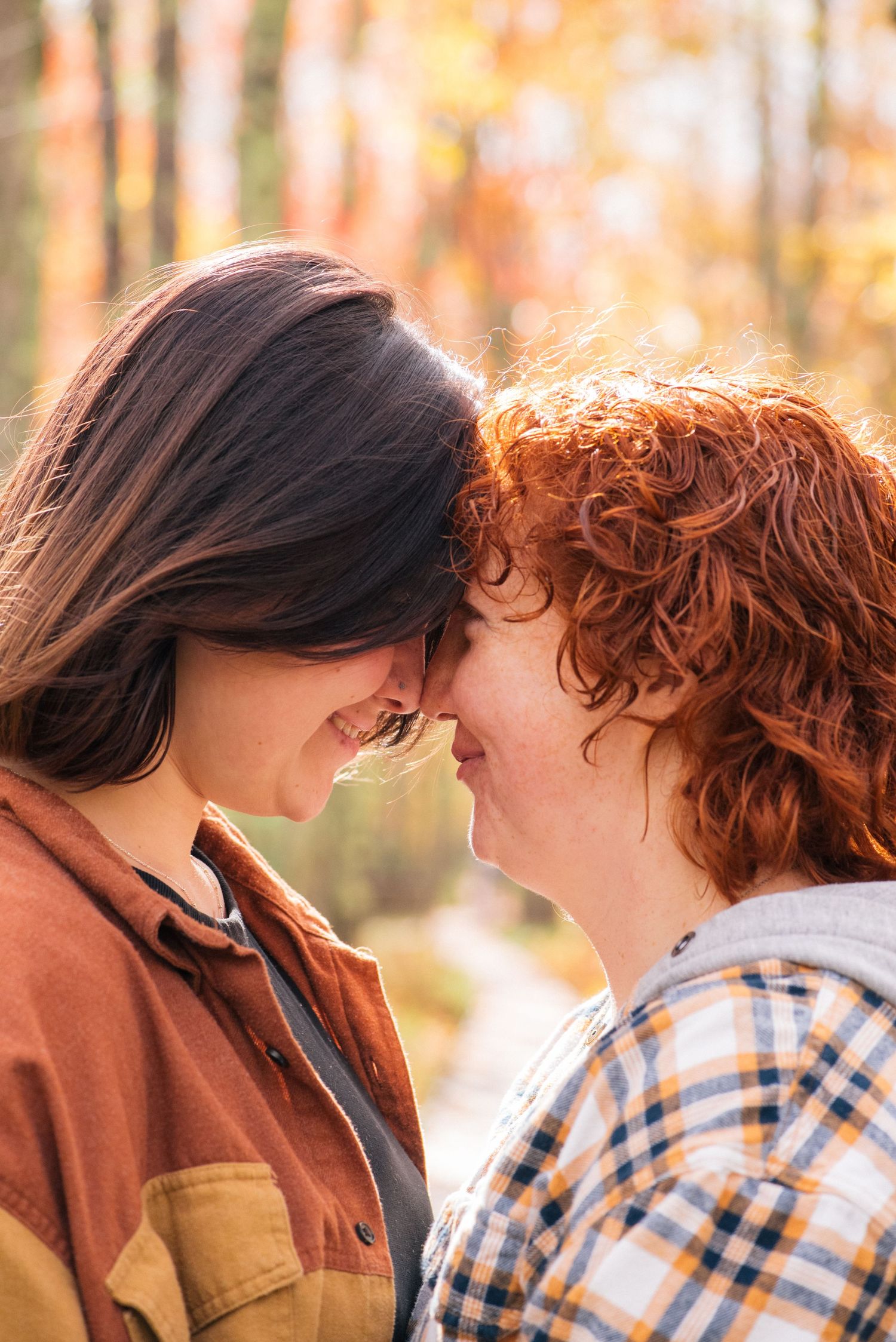 Two women smiling and touching foreheads in an autumn forest setting.