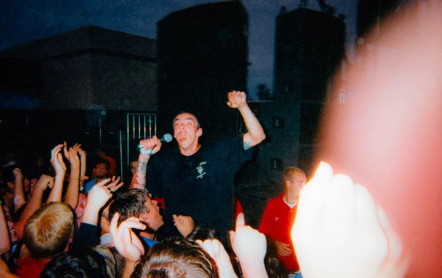 Shirtless man crowd surfing with fist raised at an outdoor punk rock concert event.