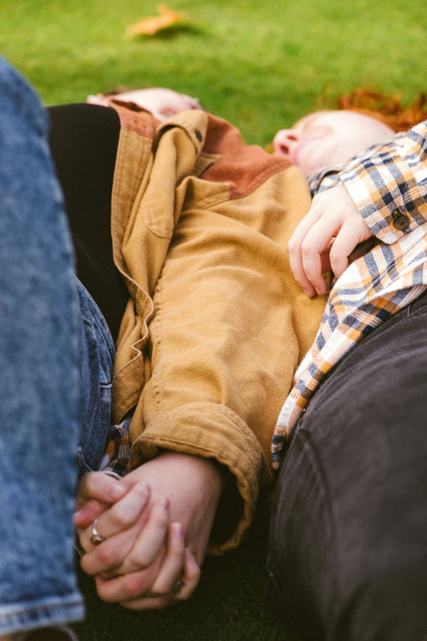 Two parents lying on grass holding hands with a red-haired child resting between them outdoors.