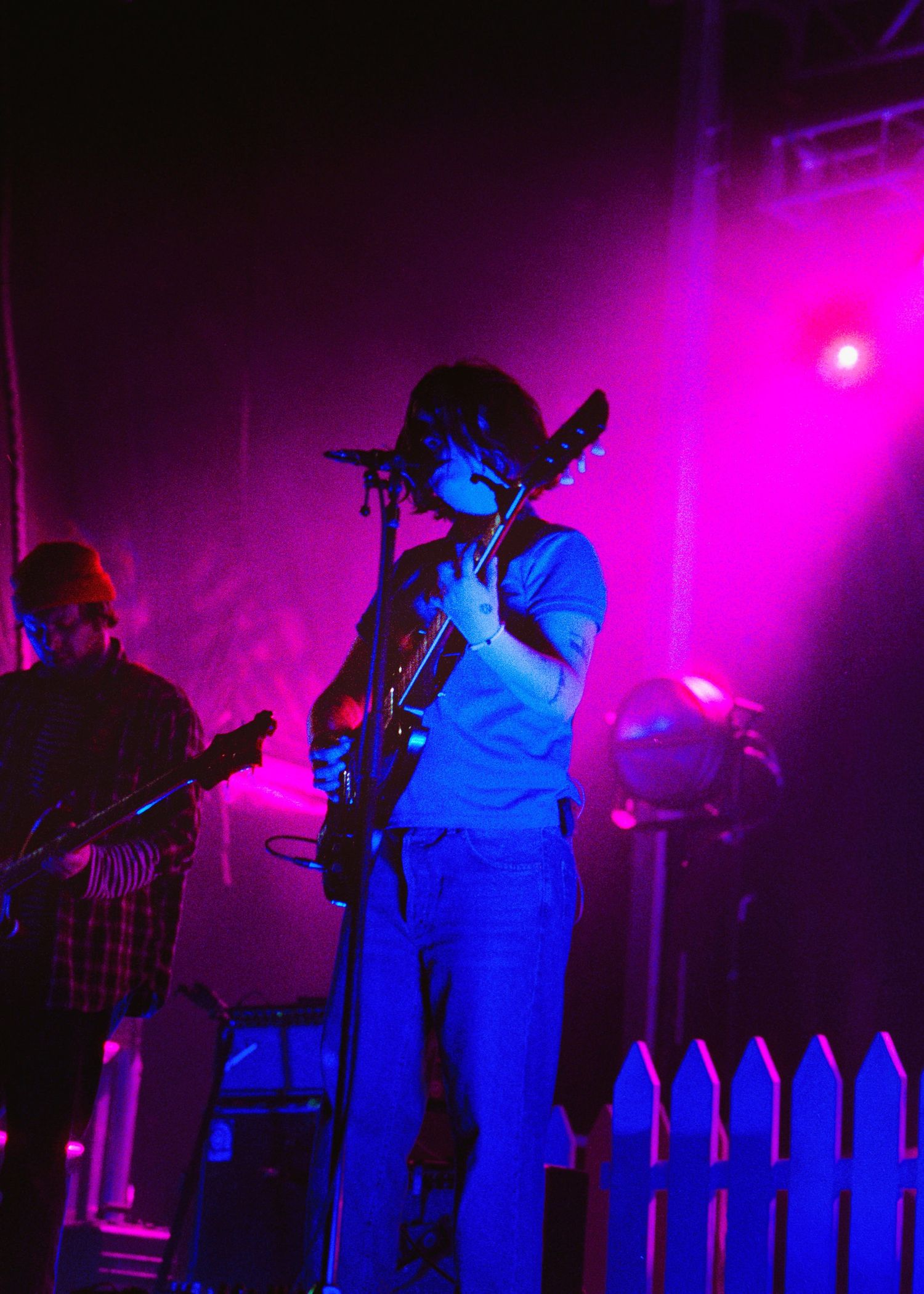 Musician playing electric guitar on stage under blue and pink lights wearing a cowboy hat at a live concert.