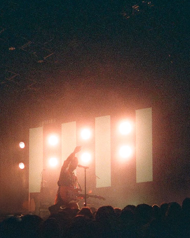 Performer silhouette raises arm on stage with warm glowing rectangular light panels and fog at live show.