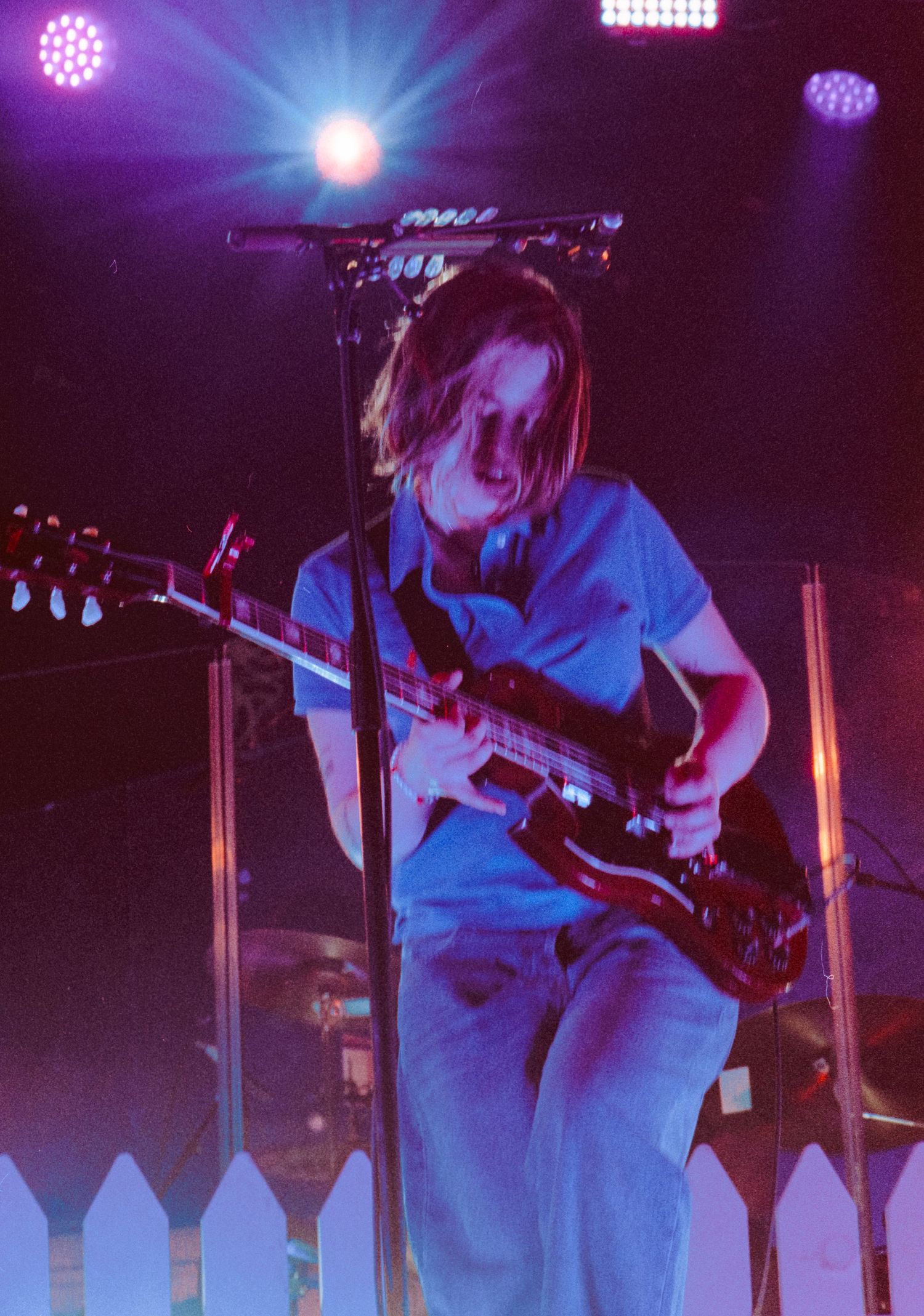 A young guitarist performs on stage under colorful lights, playing an electric guitar in a blue shirt.