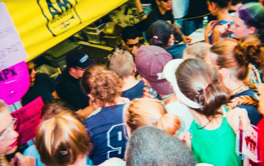 Dense crowd of festival attendees gathered around a merchandise or activity booth at Warped Tour.