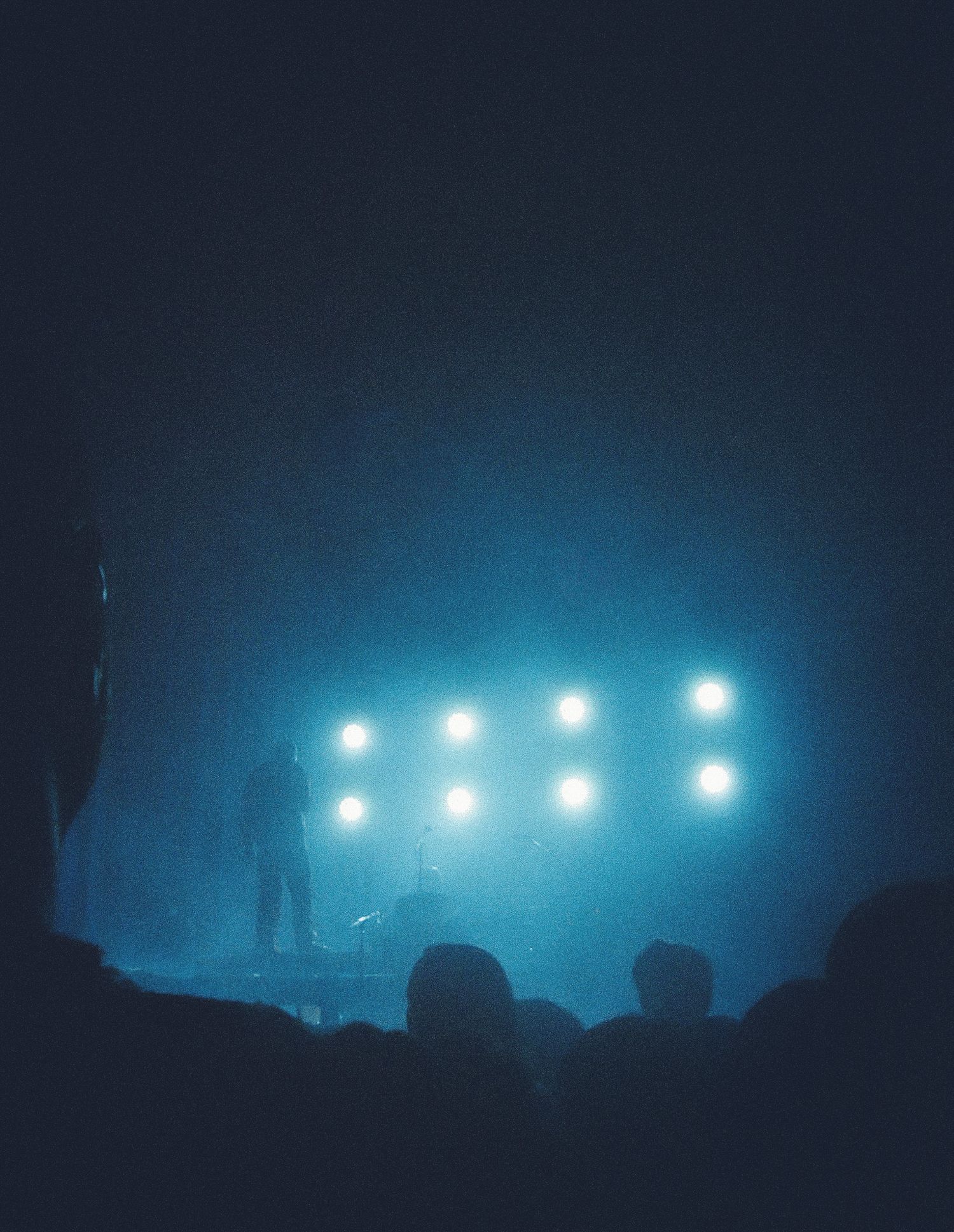 Silhouette of performer on stage with blue atmospheric fog and bright grid of lights at a concert.