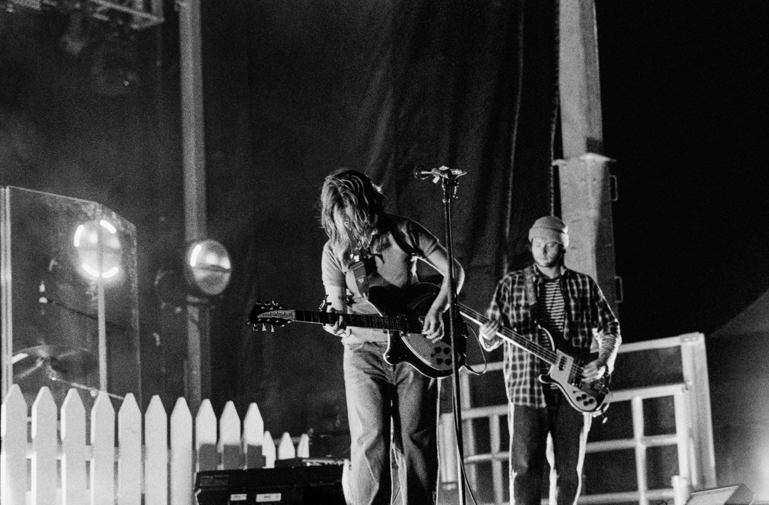 Black and white photo of two guitarists performing on stage at a live rock concert with dramatic lighting.