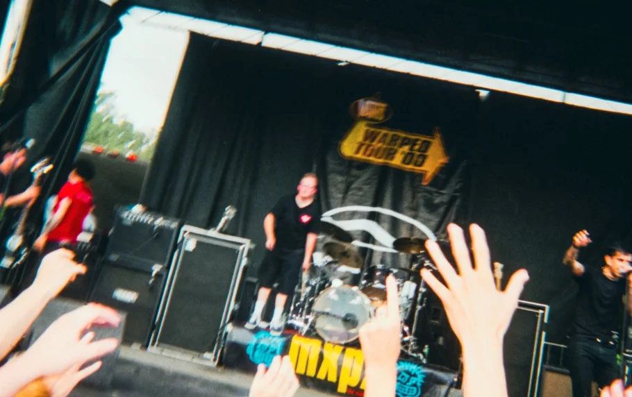 Performer on Warped Tour stage reaching toward crowd with hands outstretched toward the stage.