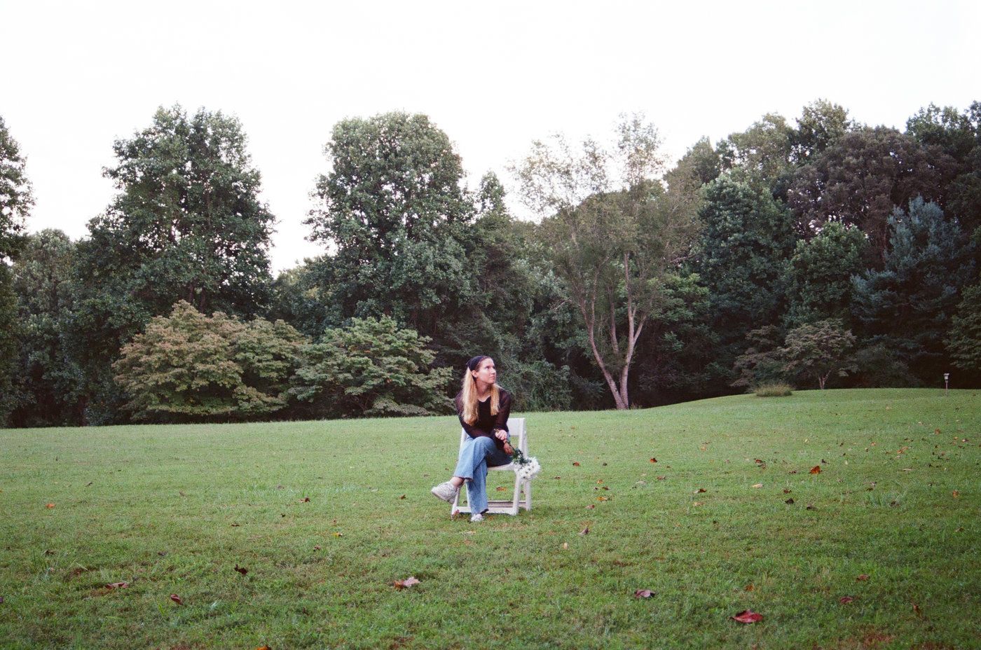 Couple embracing and dancing together on a lush green lawn surrounded by tall trees in a park.