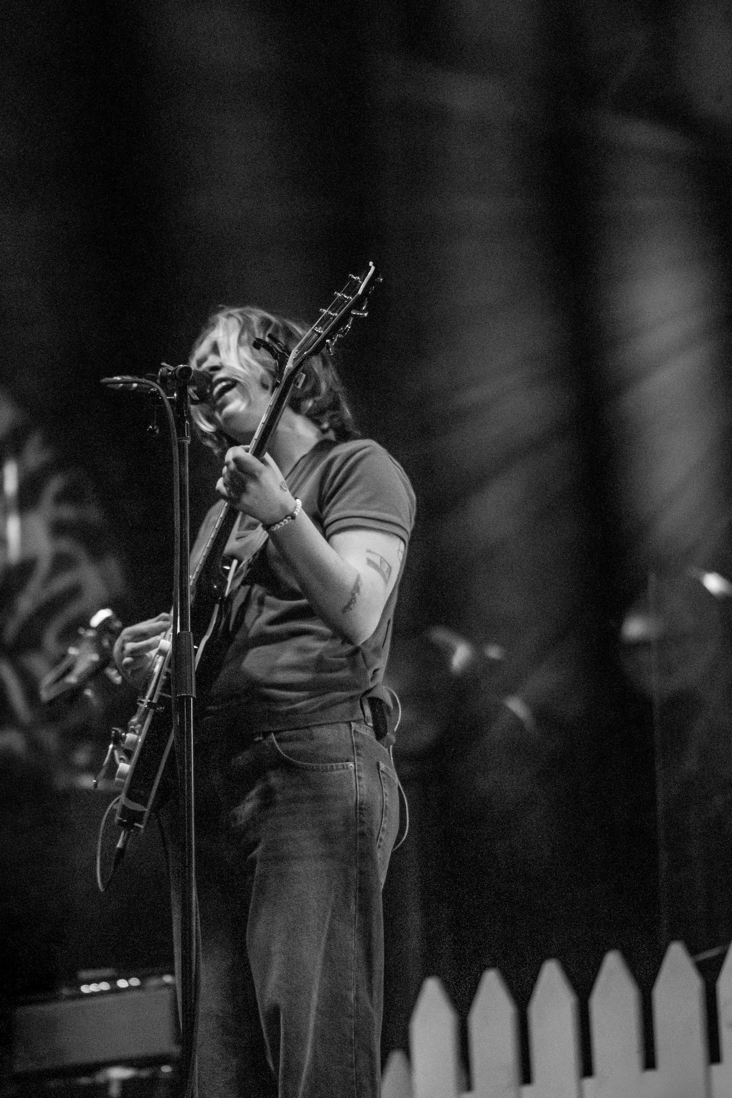 Black and white photo of a musician playing guitar and singing into a microphone on stage during a live concert.