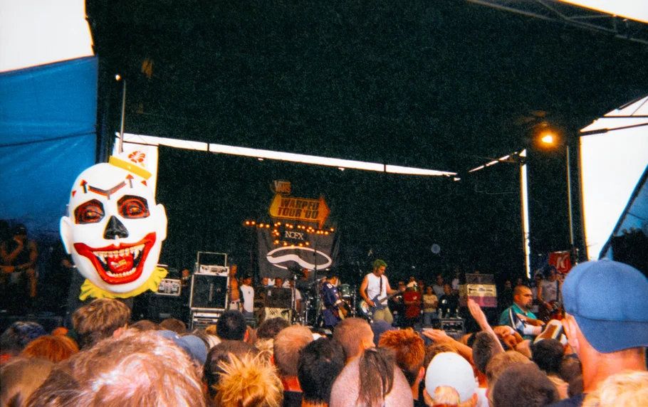 Band performing on outdoor festival stage with giant clown skull balloon floating above the crowd.